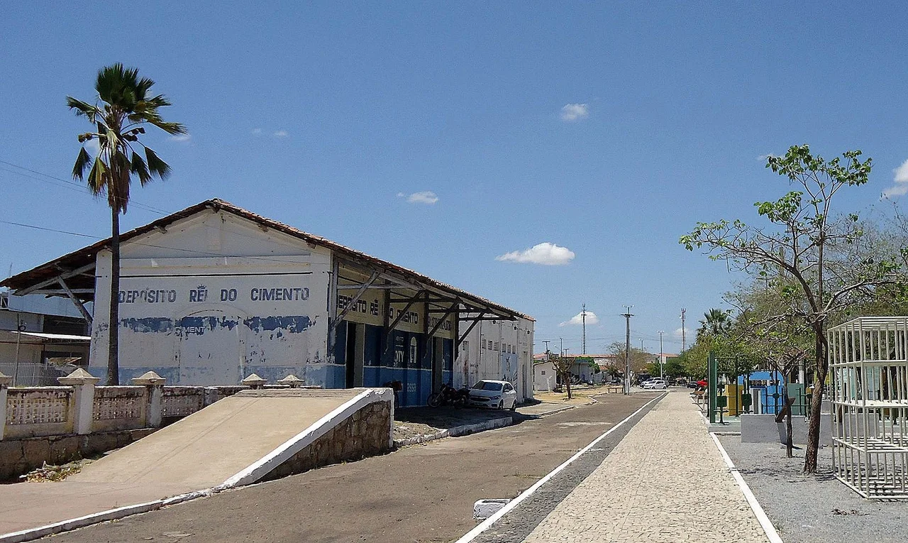 Bem ferroviário valorado/tombado pelo IPHAN na cidade de Crateús, Ceará, Brasil. Edificação do complexo da estação ferroviária Cratheús, inaugurada em 1912 na Linha Norte da Rede de Viação Cearense. Atualmente concessionada, a linha atende a Ferrovia Fortaleza-Teresina. O prédio do armazém abriga a Academia de Letras de Cratheús e um depósito de cimento. Vista geral a partir da Praça Gentil Cardoso, sentido Fortaleza.
