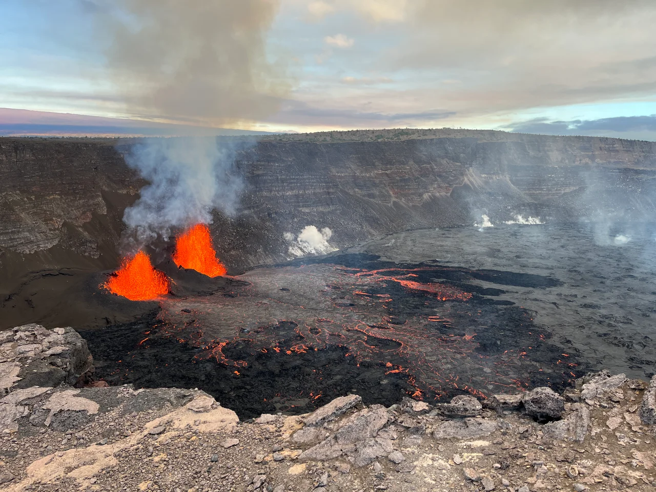 View of the Kīlauea summit eruption in Hawaiʻi Volcanoes National Park, from the south rim of the caldera. The caldera wall behind the erupting vents is approximately 210 meters (690 feet) tall.  This morning, USGS Hawaiian Volcano Observatory field crews reported lava fountain heights of 50 meters (160 feet) and 40 m (140 feet) from north and south vents, respectively. At about 8:25 a.m. this morning, field crews reported that parts of the south vent collapsed, with an associated reduction of about half in south vent lava fountain height. Lava flow activity has remained confined to the southwest crater floor area near the active vents.
