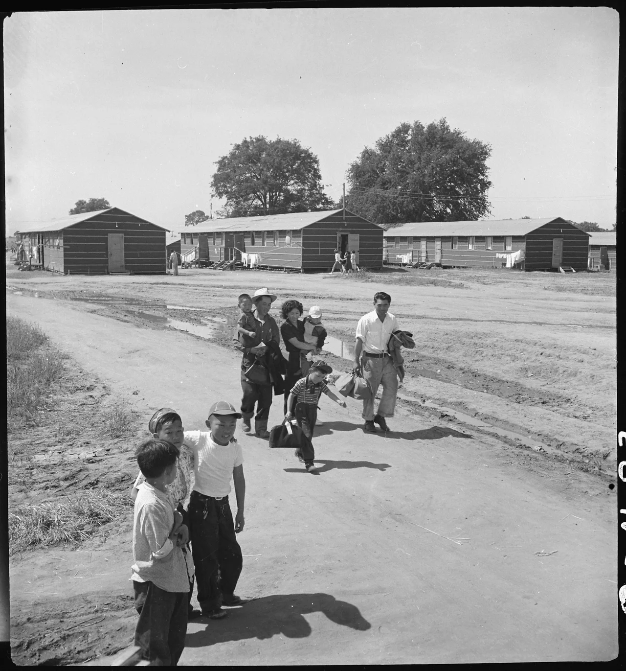 Scope and content:  The full caption for this photograph reads: Sacramento, California. Another family of Japanese ancestry has just arrived at this Center by bus. Their baggage has been inspected for contraband and they have been registered, medically examined and are now being escorted by a volunteer guide to their assigned location in the barracks.