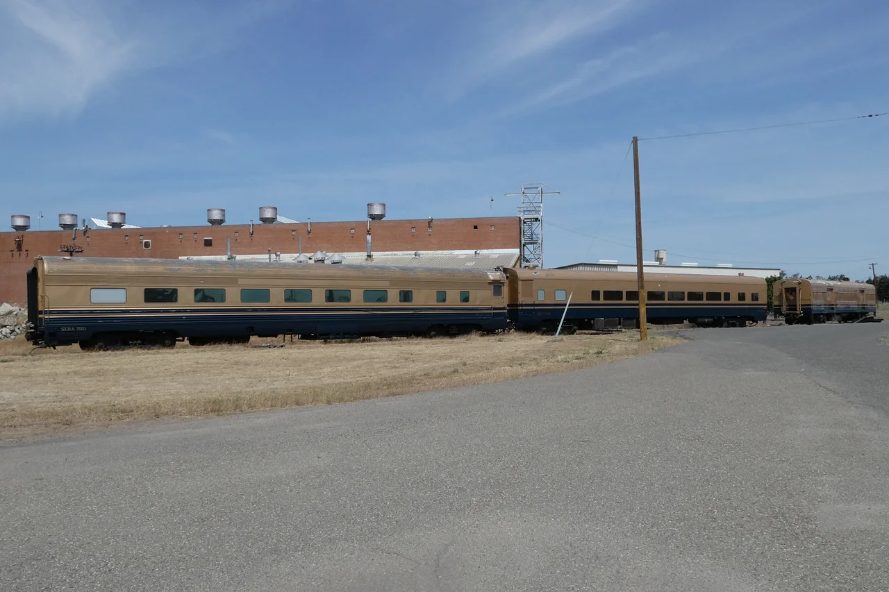Sierra Northern passenger cars #7001, #7000 "Half Dome", and an unidentified baggage car at the Riverbank Industrial Complex in May 2022