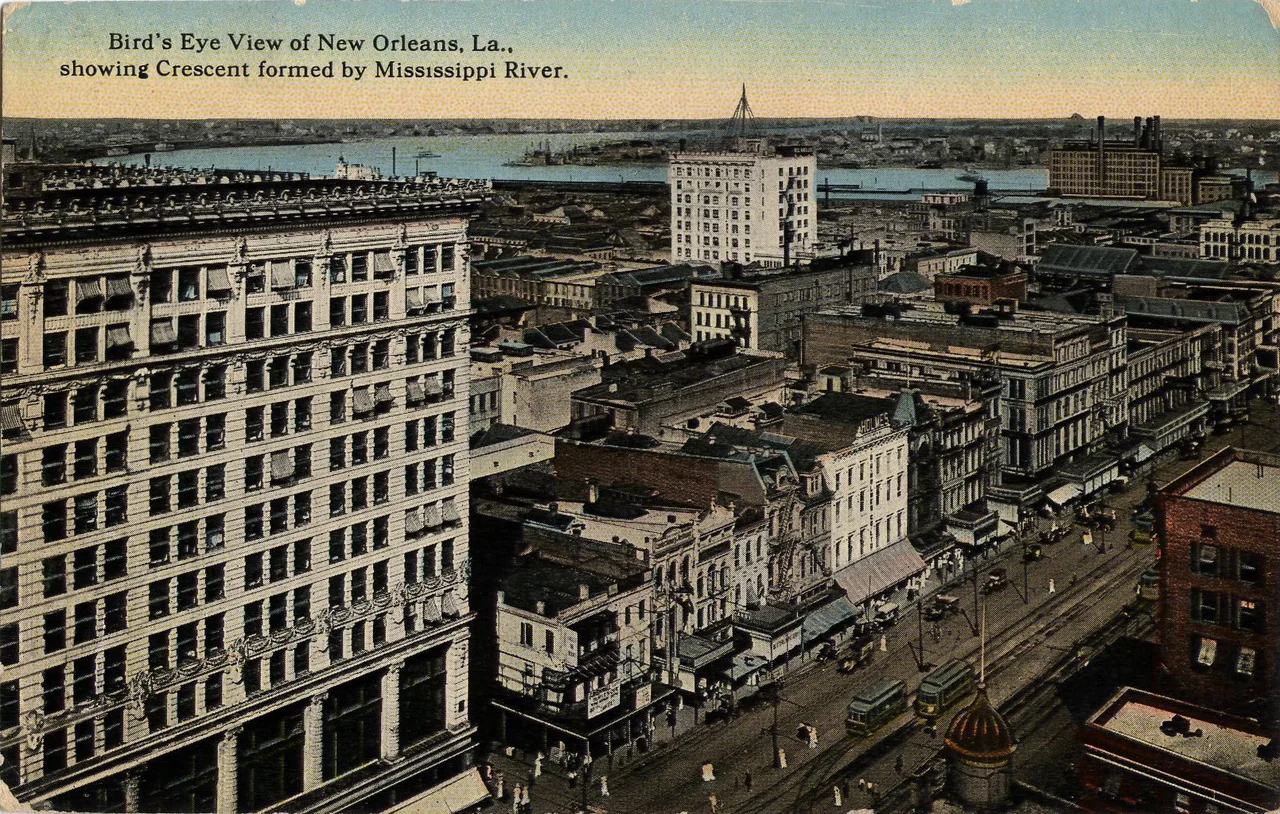 Bird's Eye View of New Orleans, Louisiana, showing the Crescent formed by the Mississippi River.
View probably taken from atop or from a high story of the Grunewald building. View looks riverwards and slightly down river. Visible are a section of Canal Street with streetcars on the neutral ground, buildings fronting Canal on the downriver side of the 800 and 700 block, a portion of the 2nd Maison Blanche Building at left, the upper French Quarter with the high-rise Monteleone Hotel, and the Mississippi River curving around Algiers Point in the background.