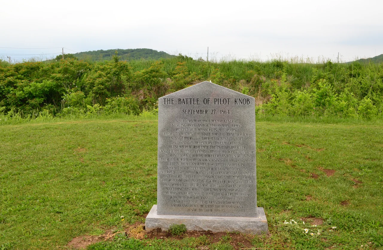 A stone memorial monument at Fort Davidson in Missouri. The earthen rampart of the fort's ruins is behind the monument.