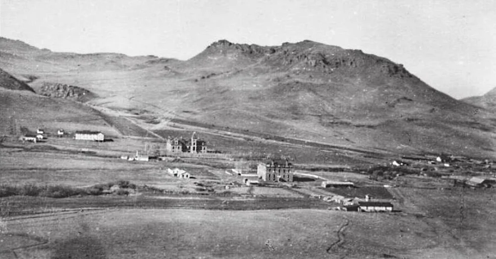 A view of St. Peter's Mission on Birch Creek (now Mission Creek) west of Cascade, Montana, in the United States. This photograph was taken prior to 1908.
Identifiable structures include the two-story wood frame boys' school (left), the Ursuline stone convent and school (center left), the opera house (center right), and original wood frame girls' school (center right low, with tower).
Catholic Jesuit priests established St. Peter Mission in 1860 on the Sun River about 8 miles (13 km) upriver from Fort Shaw, Montana. They moved the mission 2 miles (3.2 km) downstream in 1862, but this location proved difficult for agriculture. In April 1866 the mission moved again, this time to a position 2 miles (3.2 km) south Bird Tail Rock (which is 15 miles (24 km) south of the town of Simms, Montana). The mission closed almost immediately due to hostility from a nearby Native American tribe, the Piegan Blackfeet, but reopened in 1874. The mission moved again in 1881 to Birch Creek (a point 10.5 miles (16.9 km) west-northwest of Cascade, Montana). The 1881 location is depicted here. At some point between 1874 and 1881, the Jesuits built a wood frame structure to house a school for boys.
In January 1884, the new (and founding) Bishop of the Roman Catholic Diocese of Helena, Jean-Baptiste Brondel, invited the Ursuline religious order of women to join the Jesuits at St. Peter's Mission and assist them in educating the Native Americans. Five Ursuline sisters arrived in October 1884. In 1885, they built several log cabins and a wood frame structure that contained a chapel and classrooms for girls. This structure also had a two-and-a-half story bell tower. The Ursulines built a three-story stone building with basement beginning in 1892, into which the girls' school moved in 1896. This structure was funded by donations from the future Saint, Katharine Drexel, a Philadelphia, Pennsylvania, heiress. This building also served as the nuns' convent. Over time, the Jesuits and Ursulines built a bakery, barn, corral, laundry, and workers' housing. The Ursulines—who believed in music and art training as well as education in reading, math, and science—also built an opera house at St. Peter's in 1896. The Jesuits stopped educating boys, turning that function over to the nuns.
The boys' school closed in 1896, and fire destroyed it in 1908. The Ursulines moved their school into nearby Great Falls, Montana, in 1912. Fire destroyed the stone convent/school and the girls' wood frame school in 1918. St. Peter's was largely abandoned afterward.
The ruins of St. Peter's Mission remained a popular tourist spot for many decades. As of 2010, only the foundations of a few structures remained at St. Peter's.