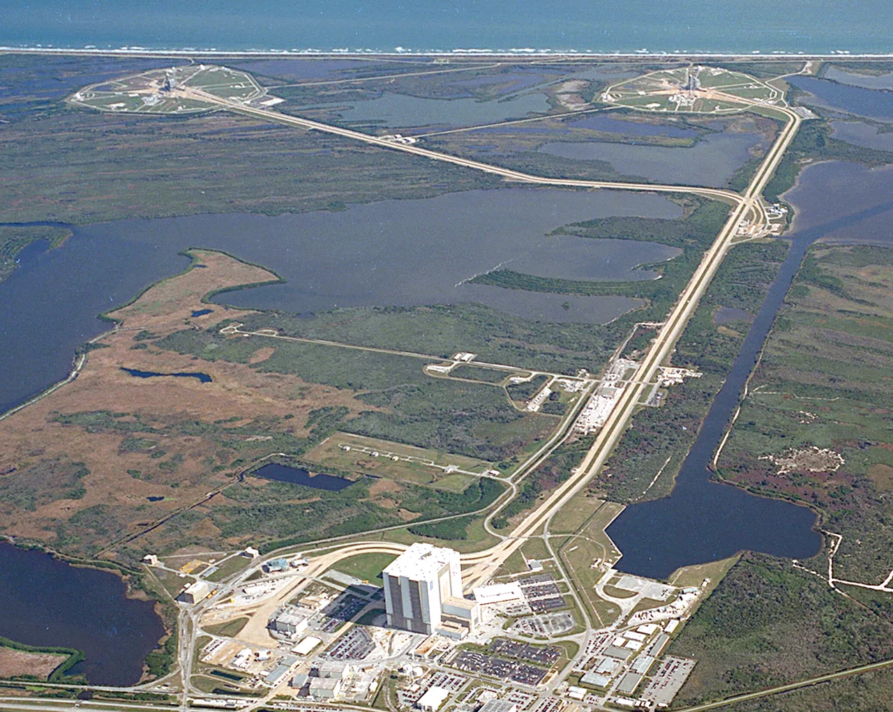 KSC's Launch Complex 39 is strategically located next to a barge site and a variety of structures, including a Vehicle Assembly Building (VAB), Orbiter Processing Facilities (OPF), Press Site, Launch Control Center (LCC), and a crawlerway to the pads. 
The crawlerway, leading to pads 39B on the left and 39A on the right, can be seen extending from the massive VAB at the left in this photo. The VAB, which covers eight acres and stands 525 feet tall, is used for assembly, stacking and mating of Space Shuttle elements. Originally built for assembly of Apollo/Saturn vehicles and later modified to support Space Shuttle operations, the VAB is one of the largest buildings in the world. 

The LCC, seen here as the small white building to the upper right of the VAB, is where launch, mission support, and loading are controlled.