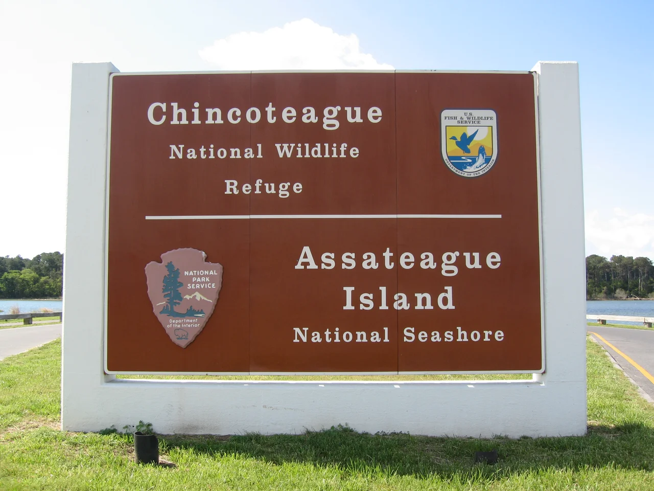 Chincoteague National Wildlife Refuge / Assateague Island National Seashore monument sign located at entrance to Assateague Island, Virginia.  The Assateague Channel is in the background.  Photograph taken in May 2008 from Maddox Boulevard facing southeast, showing the northwest face of the sign.