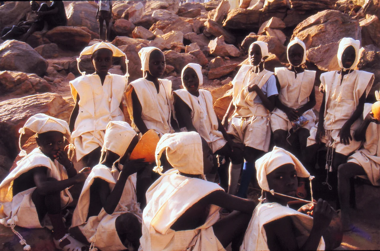 Eleven boys in white clothing with bonnets at Tireli market, just after circumcision, Mali 1990