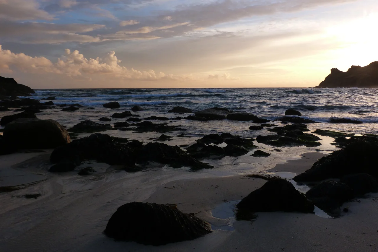 Nanjizal beach at sunset, looking out to sea. Carn Boel headland is visible on the right. Tide is ebbing, with low tide a couple of hours in the future.