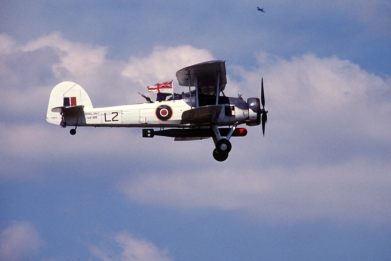 A Royal Navy Fairey Swordfish Mk. II (serial number LS326) in flight during Air Fete'88, a NATO aircraft display hosted by the U.S. Air Force's 513th Airborne Command and Control Wing, at RAF Mildenhall, Suffolk (UK). This aircraft is today operated by the Royal Navy Historic Flight.

RN description: This aircraft was built in 1943 at Sherburn-in-Elmet. Later that year she was part of 'L' Flight of 836 Squadron on board the MAC ship Rapana, on North Atlantic Convoy duties. Following her active service she was used for training and communications duties from the Royal Naval Air Station Culham near Oxford and Worthy Down near Winchester. In 1947 Fairey Aviation bought LS326 and displayed her at various RAeS Garden party displays. The following year she was sent to White Waltham for storage and remained there getting more and more dilapidated until Sir Richard Fairey gave orders for the aircraft to be rebuilt. The restoration work completed in October 1955 and thereafter she was kept in flying condition at White Waltham registered as G-AJVH and painted Fairey Blue and silver. In 1959 LS326 was repainted for a starring role in the film 'Sink the Bismarck!'. In October 1960 she was presented to the Royal Navy by the Westland Aircraft Company and has been flown ever since. For many years she retained her "Bismarck" colour scheme and in 1984 D-Day invasion stripes were also added for the 40th Anniversary celebrations when she overflew the beaches of Normandy. Since 1987 she has worn her original wartime colour scheme for North Atlantic convoys with 'L' Flight of 836 Squadron. Following extensive work by BAeS Brough to her wings, it is hoped to have LS326 back in flying condition again in 2008.