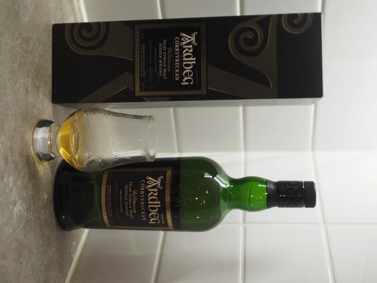 A bottle of Ardbeg Corryvreckan single malt Scotch whisky with its decorative and protective casing, with a small amount of the whisky poured into a whisky glass.