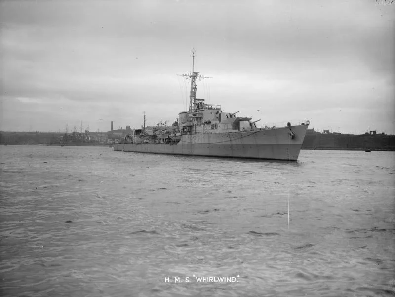 British destroyer HMS Whirlwind underway, near some docks.