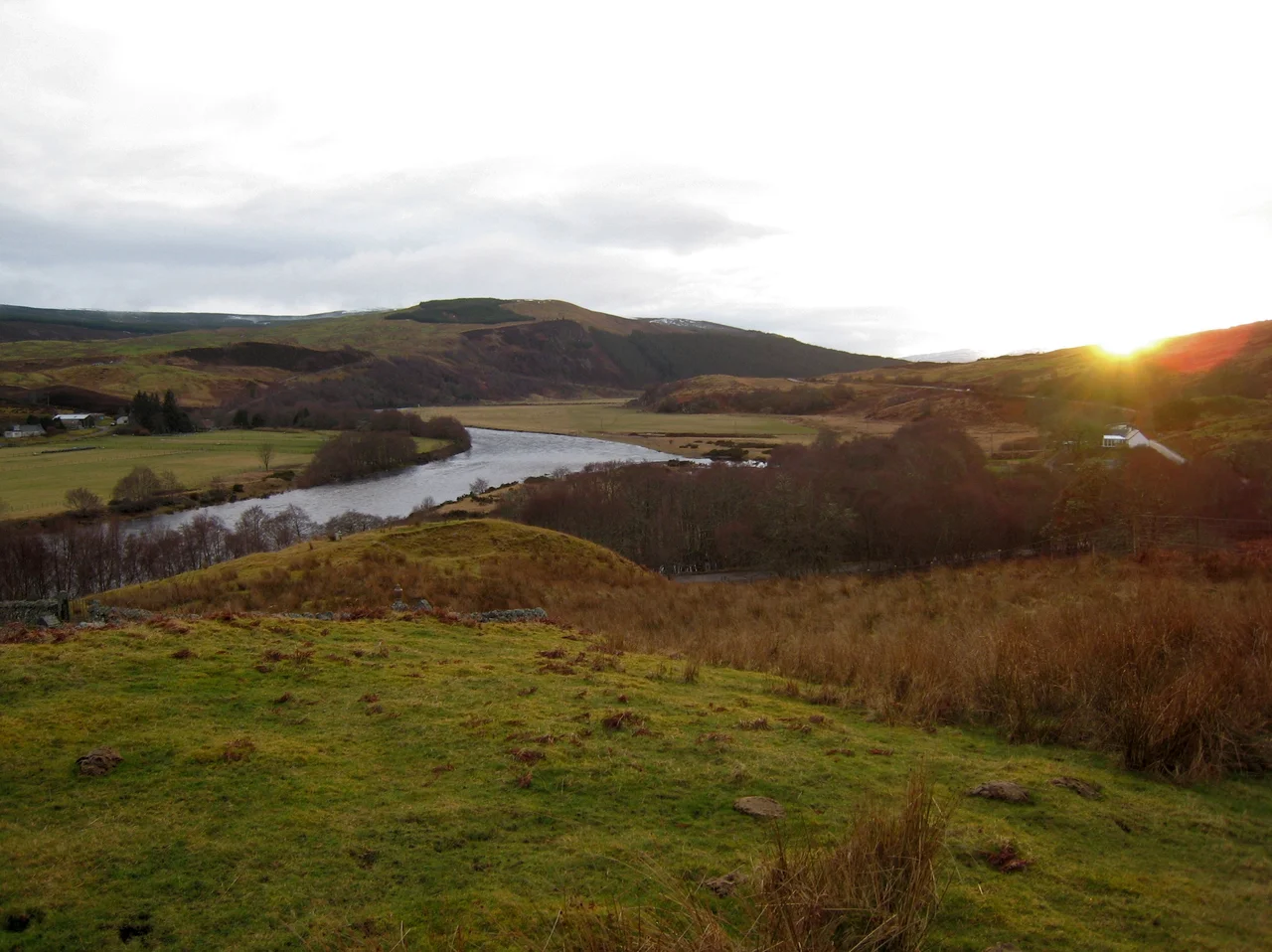 View of Strathoykel in northern Scotland looking west (upstream) from Tutim cemetery at sunset. The cemetery wall is in the foreground, Brae farm on the left of the photo, and Tuiteam house on the right. The mouth of the Tutim Burn can be seen entering the River Oykel roughly level with Tuiteam house. The hill is Ben Chreagach. The site is notable for the en:Battle of Tuiteam Tarbhach which took place around Tuiteam house in about 1406.