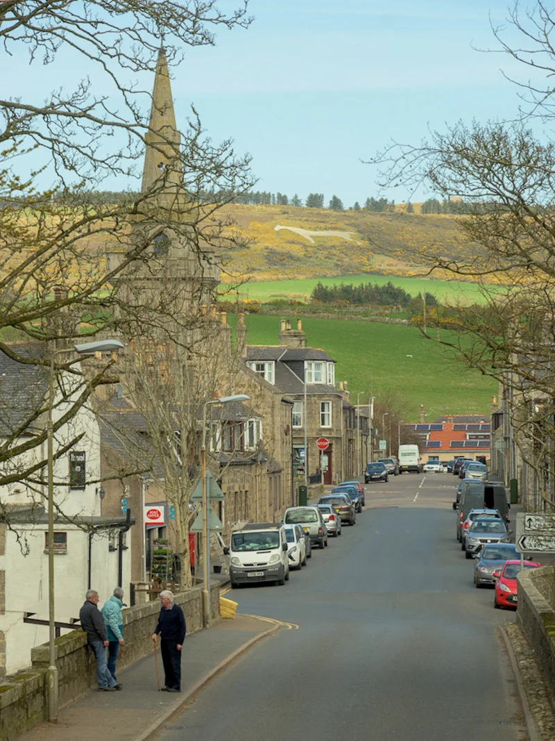 View of the White Horse of Mormond Hill from Bridge Street, Strichen. Cropped and retouched by the uploader.