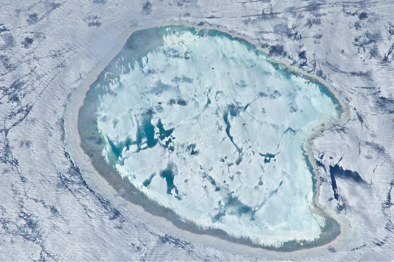 This photograph of the Bassas da India, an uninhabited atoll in the Indian Ocean, has an almost surreal quality due to varying degrees of sunglint. In this image, the presence of currents is highlighted as darker patches or streaks (image left and upper right). In contrast, shallow water in the lagoon presents a more uniform, mirror-like appearance, suggesting that there are no subsurface currents. Wave crests visible around the atoll are likely the result of both surface winds and subsurface currents.