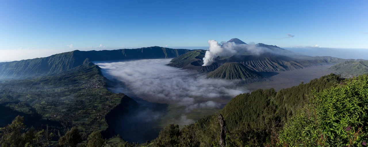 This panoramic photo depicts the Tengger Caldera and Mount Bromo Volcano, set amidst the Tengger Massif Volcano Complex in East Java, Indonesia. The panorama was created by taking seven vertical shots and stitching them together via Lightroom 6. The series of photos were taken from the top viewpoint of a nearby mountain, following a hike up from Cemoro Lawang hamlet to witness the sunrise. This beautiful landscape is officially part of the Bromo-Tengger-Semeru National Park.