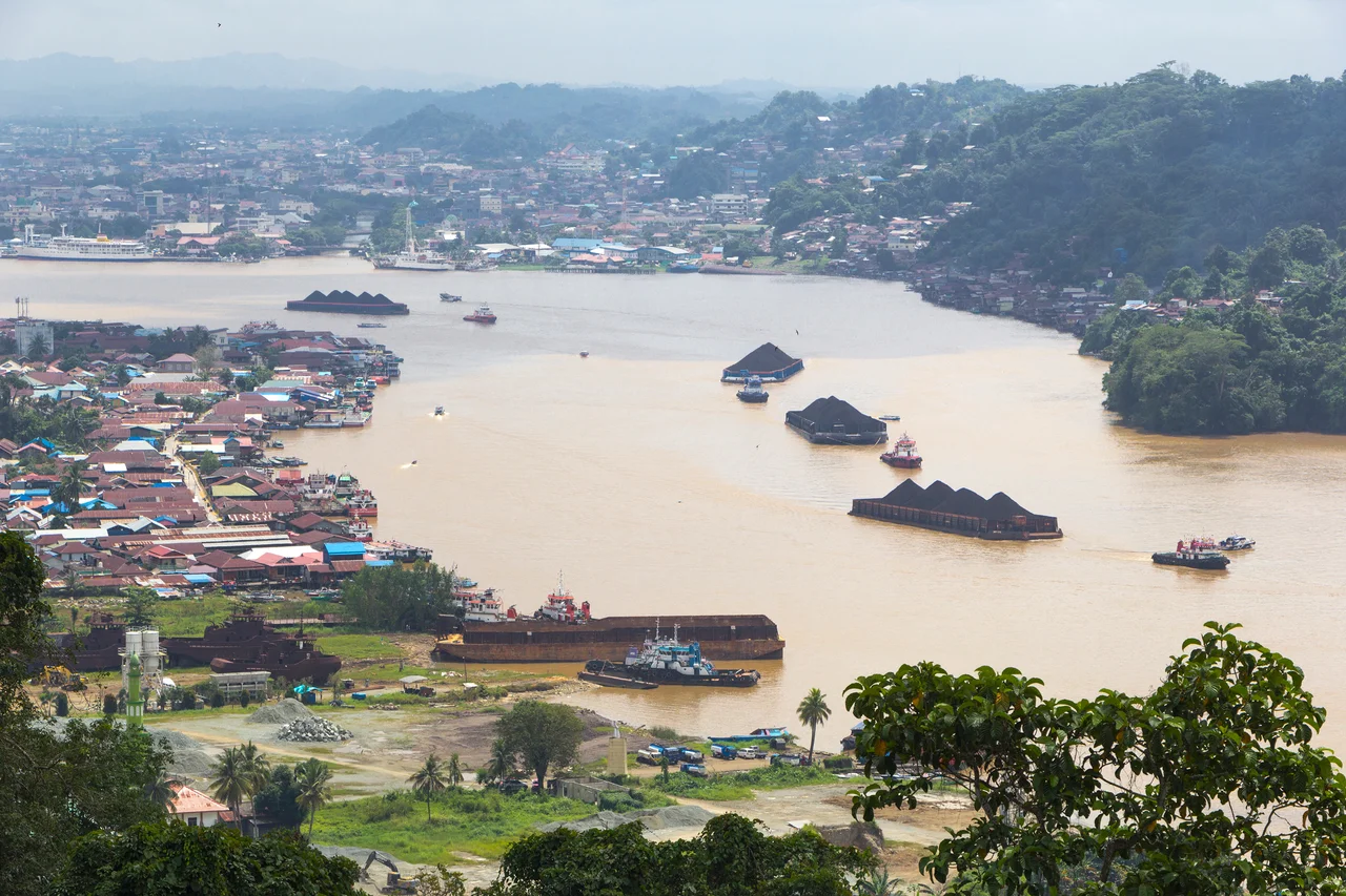 Barges with large tonnage loaded with coal and other goods pass by on the Mahakam river, Samarinda City, Indonesia.