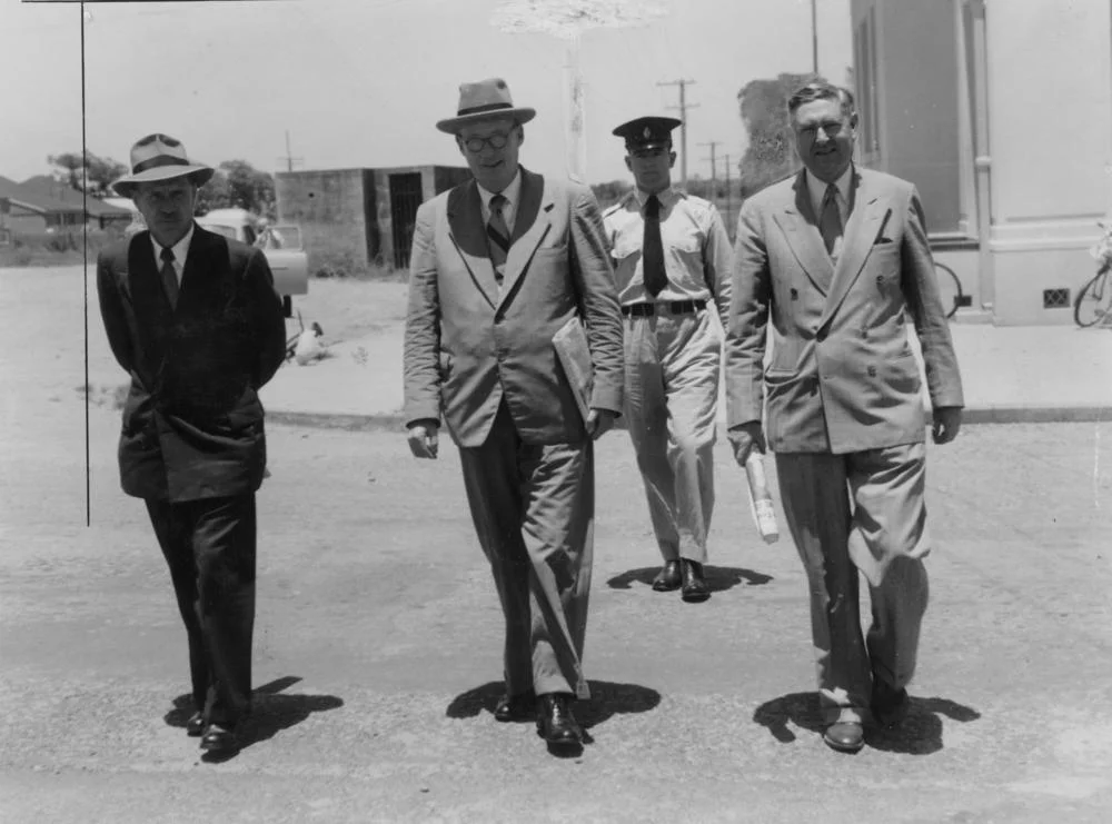 Members of the Collinsville Royal Commission, 1954
Members of the Royal Commission are being escorted by Constable Gordon Duncan at Bowen, during a break in proceedings. The members pictured are Walter Scott, Justice Sheehy (chairman) and Septimus Flowers. (Description supplied with photograph.).
The Royal Commission was being held into the cause of a 1954 poison gas explosion at Collinsville State Coal Mine which claimed seven lives.