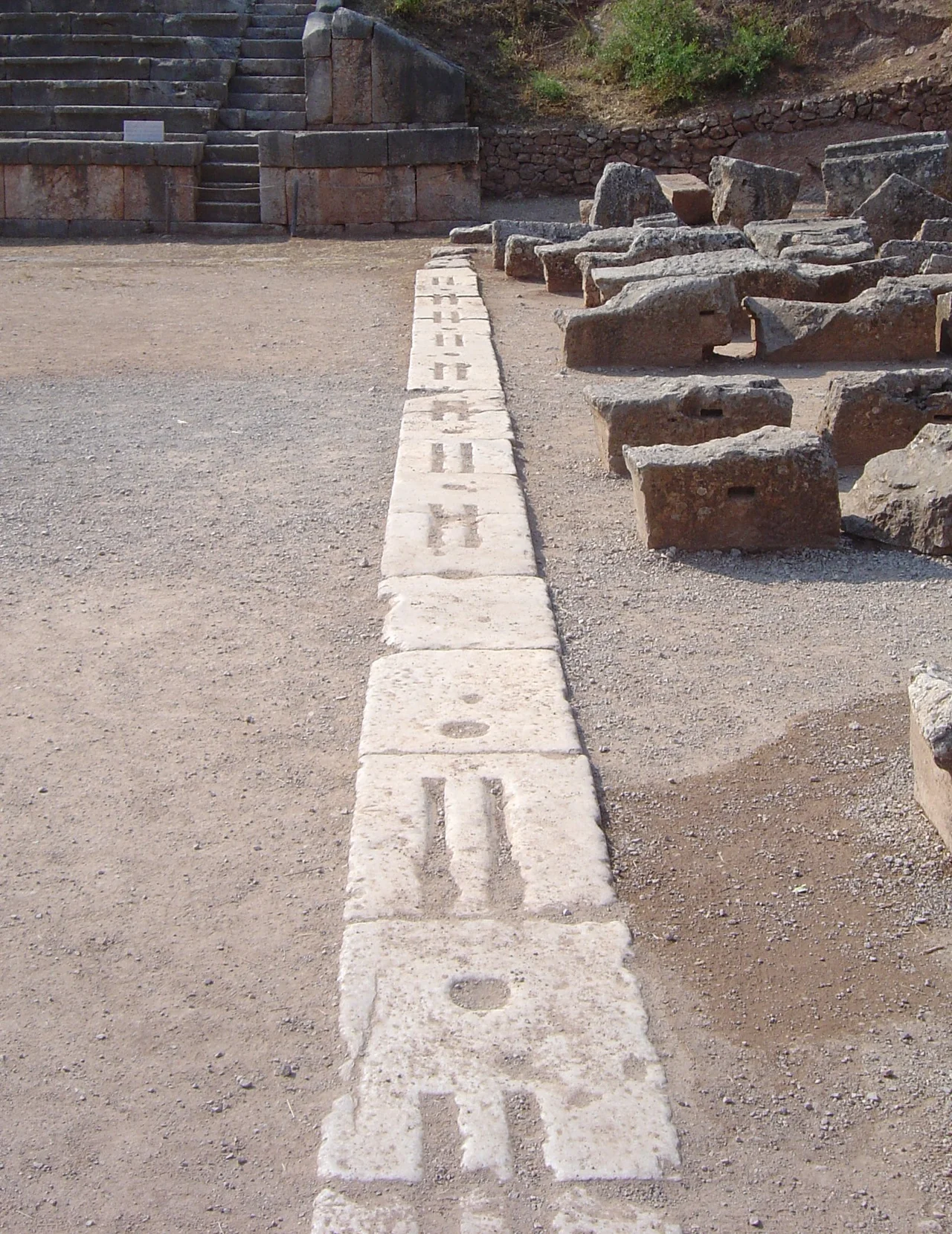 The starting line at the stadium used for the Pythian Games at Delphi, Greece.  This starting line has a design representative of that of many ancient Greek stadiums: stones with two lines in which the athletes nudged their toes, and round holes in which posts could be erected to support the start signalling mechanism.
The stone steps for sitting the public behind were erected under the Romans.