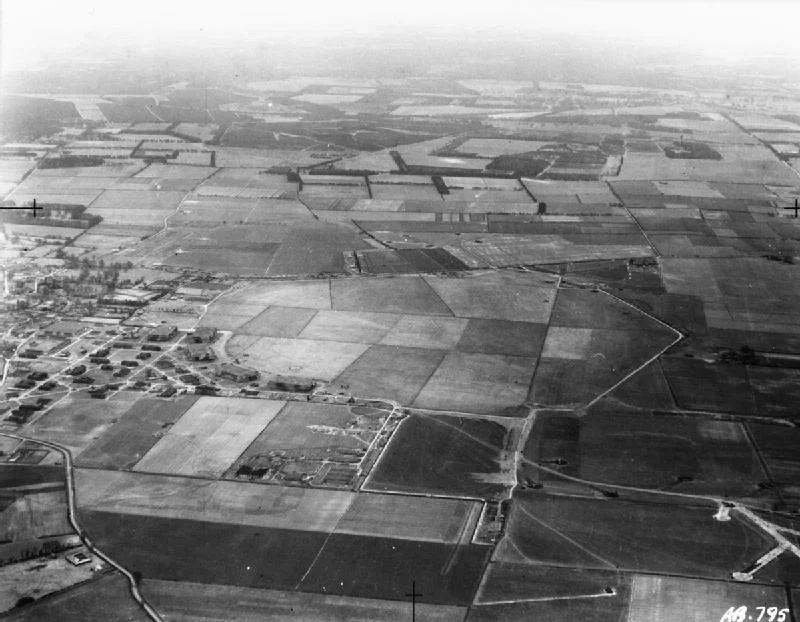 IWM caption : Oblique aerial view of RAF Feltwell, Norfolk, seen from the west, looking to the Breckland beyond. Vickers Wellingtons of Nos, 57 and 75 (New Zealand) Squadrons RAF can be seen parked in front of the hangars and on the airfield perimeter, as well as on pan-shaped hard-standings in the adjoining fields.