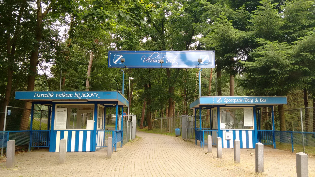 De entree van Sportpark Berg &amp; Bos van voetbalclub AGOVV (Apeldoorn). Teksten: 'Hartelijk welkom bij AGOVV', 'Veluws Trots', 'Sportpark "Berg &amp; Bos"'.