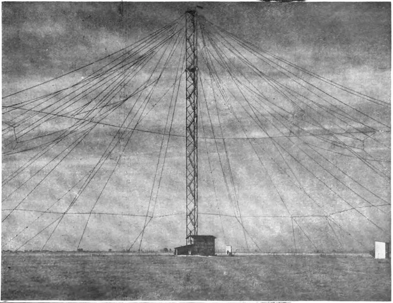 A large umbrella antenna used as the transmitting antenna for the transatlantic wireless telegraphy radio station, Nauen Transmitter Station,   built by Gesellshaft fur Drahtlose Telegraphie at Nauen, Germany in 1906, which served as Germany's main communication channel with other nations during World War 1.  It consisted of a steel truss tower 100 meters (328 feet) tall, insulated from the ground, attached to the transmitter, with a radial network of cables extending diagonally from the top, anchored to the ground at a distance of 200 m from the tower.  The bottom end of the 162 umbrella cables were attached to the three ground anchors with hemp ropes, so the umbrella was insulated from the ground.  The surface area of the umbrella was 60,000 square meters (646,000 sq. ft. or about 15 acres). The Nauen spark transmitter had an input power of 35 horsepower (26 kilowatts) and radiated in the very low frequency band.    The vertical tower served as an electrically short monopole mast radiator and the radial cables served as a capacitive top load to increase the current in the radiator.  The other side of the transmitter was connected to a ground (Earth) system consisting of 108 buried cables radiating from the tower, covering 126,000 square meters or about 31 acres.