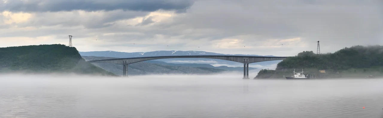 A view to foggy Dagsvikbukta which is part of Sundet (Vefsnfjorden) in Leirfjord, Nordland, Norway. Fv220 road crosses the water to Alsta by the Sundøy Bridge on the right. Photographed in 2011 June.