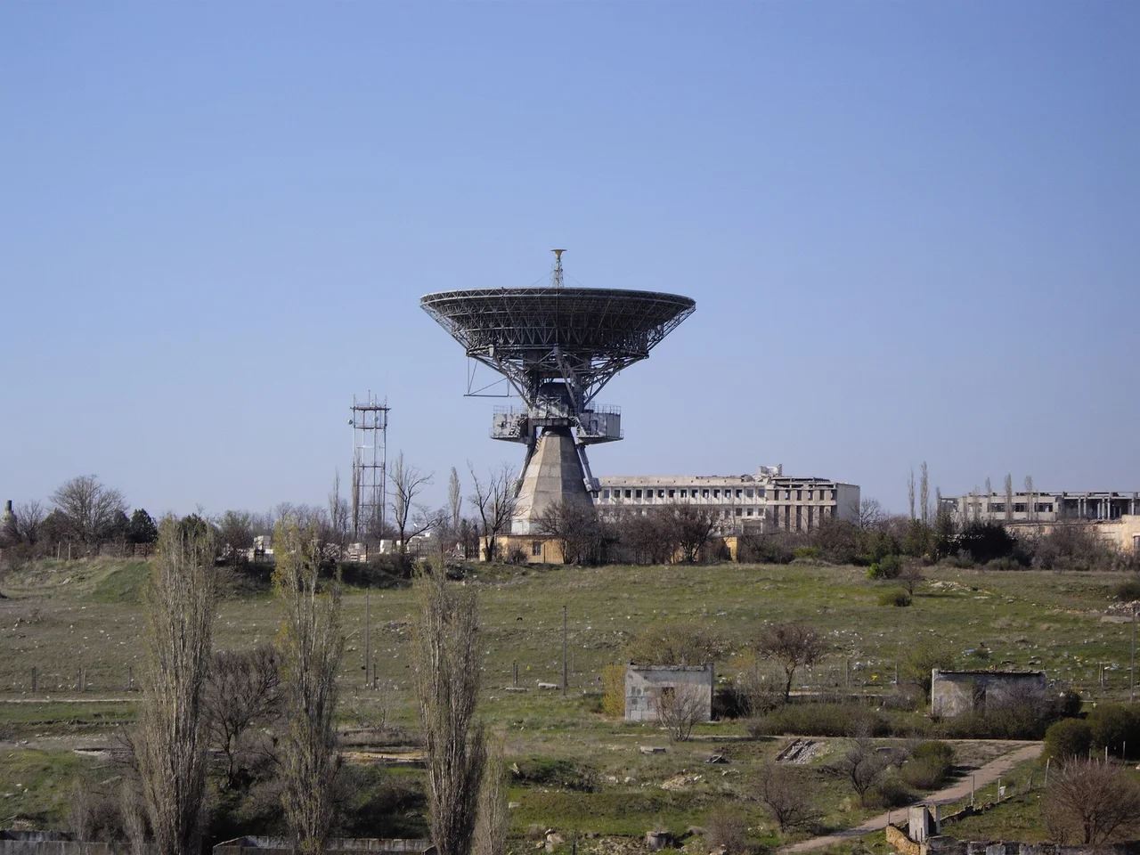 This component is located in the southern portion of the main operations area. It consists of a 105-foot tracking dish mounted on an azimuth/elevation pedestal, a large U-shaped control building, control/support buildings, and several small support buildings. Adjacent to the antenna and on two sides arc rosette patterns of devices/structures which are used when the dish has been lowered for maintenance or modification. A crane used to lower and erect the dish is present on the latest coverage. A 105-foot dish antenna such as this one would permit communications and telemetry reception at lunar distances. The antenna is operational. (CIA report "Simferopol Space Flight Center". June 1969 )